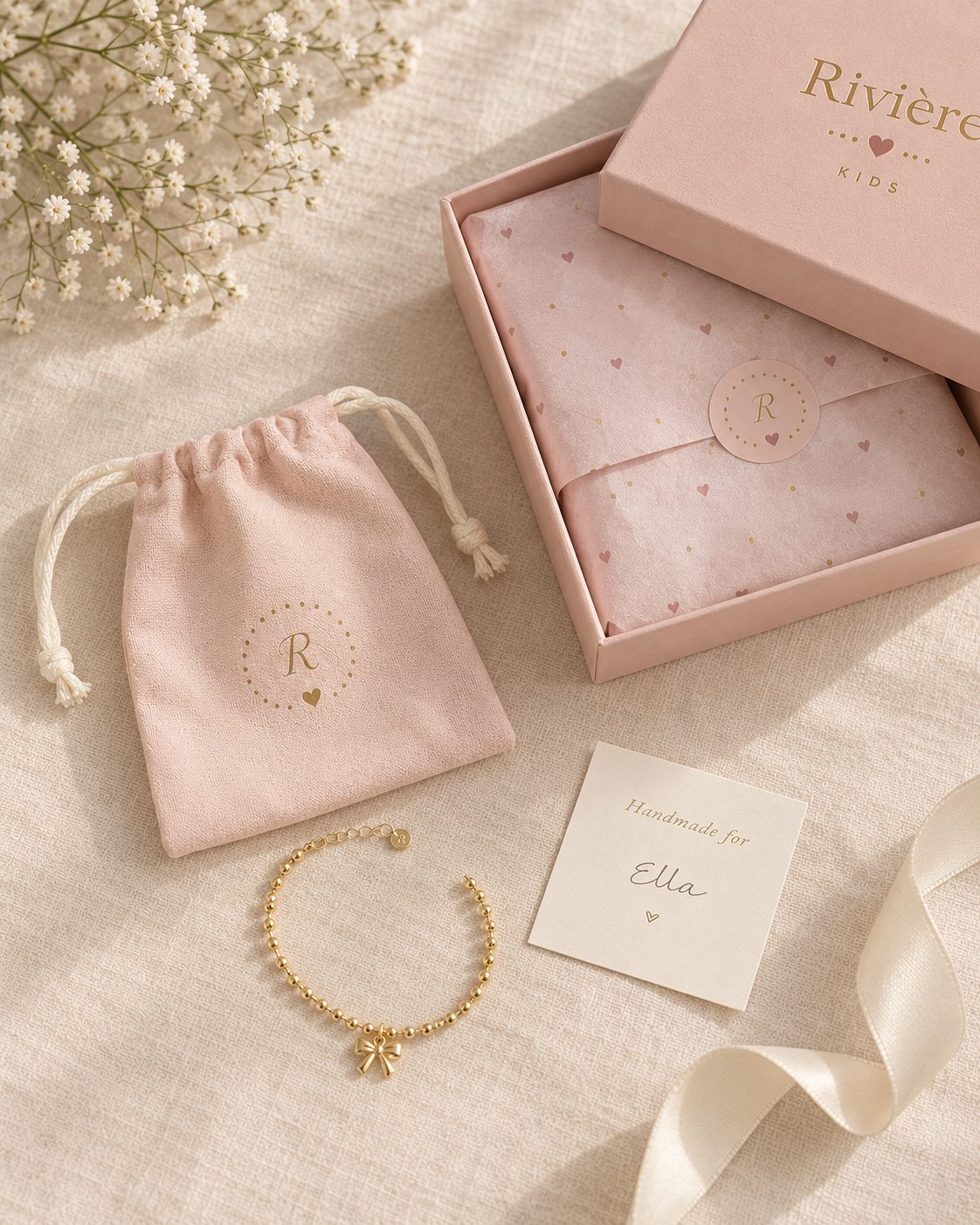 The blush Rivière Kids gift box with printed tissue, stamp sticker, storage pouch, Bow Bracelet and a Handmade for card